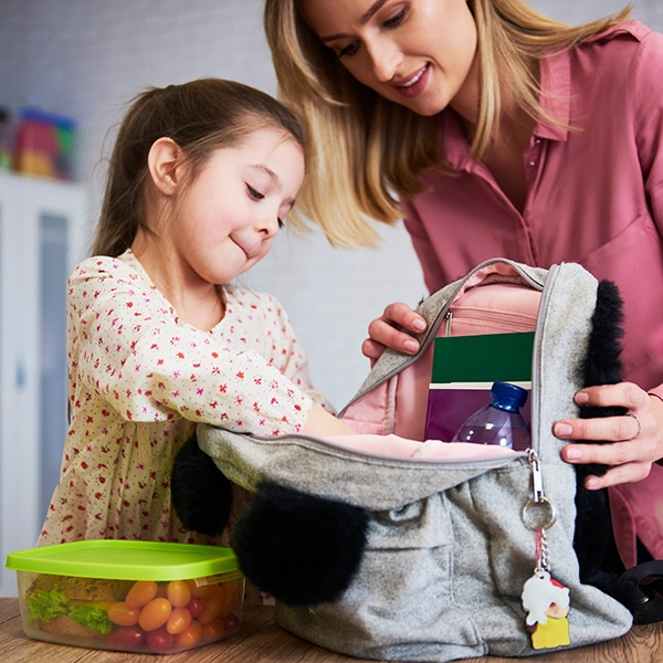 Mutter und Tochter packen die Pausenmahlzeit in den Schulranzen